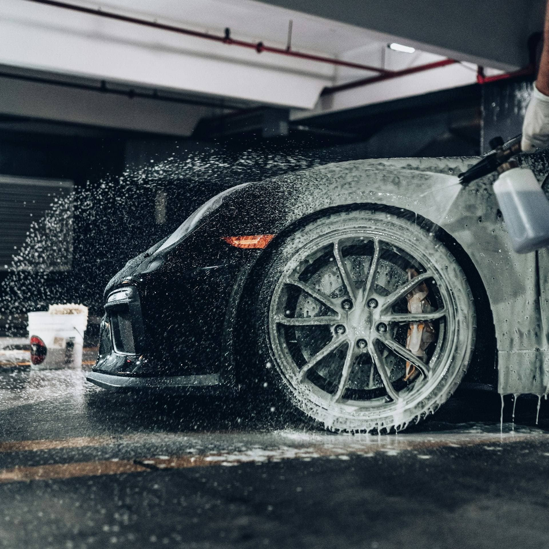 Snow foam sprayed onto a black sports car in a detailing garage